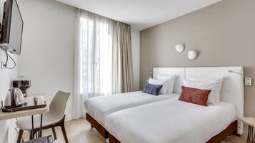 Habitación de hotel con dos camas, un escritorio con hervidor y una silla.