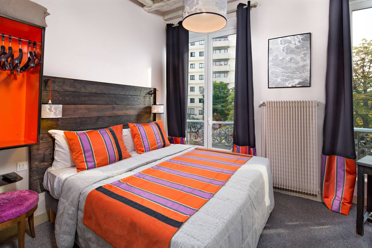 A hotel room with a large bed, a wooden headboard, a view of the city, and a window with curtains.