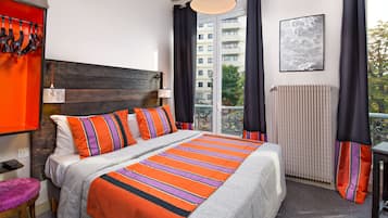 A hotel room with a large bed, a wooden headboard, a view of the city, and a window with curtains.