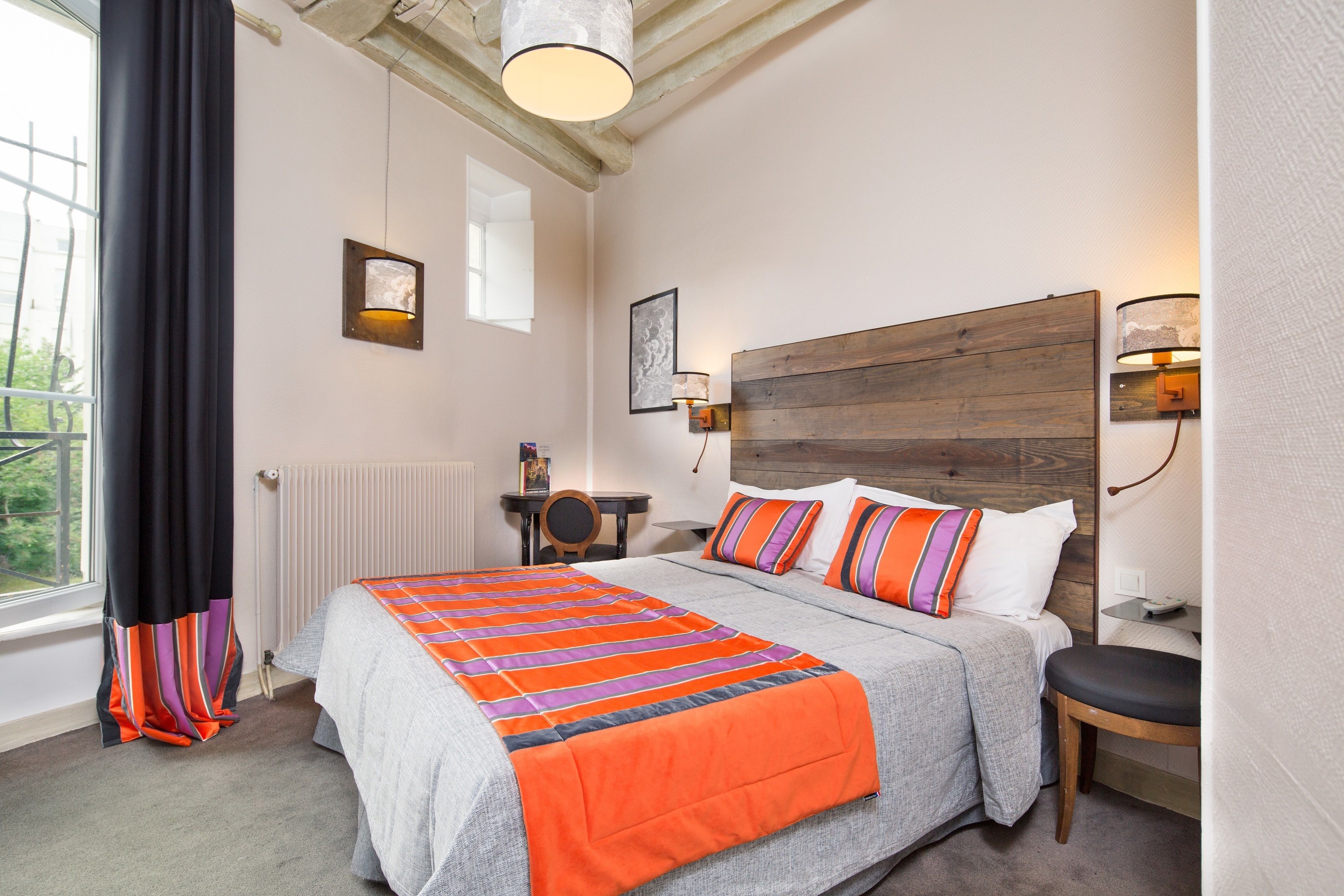 A bedroom with a large bed, a wooden headboard, a bedside table, and a window with curtains.