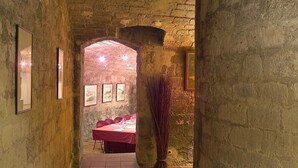 A narrow stone corridor with a tiled floor leading to a room with a red table and chairs. - Hôtel Claret Bercy (Paris)