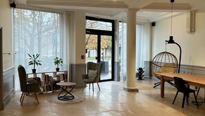 A spacious room with a large window, a wooden table, a hanging chair, and a bookshelf. - Hôtel Claret Bercy (Paris)