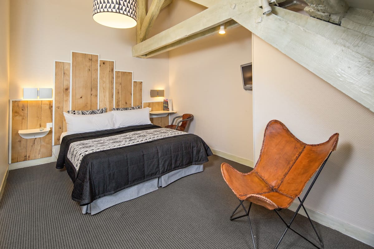 A bedroom with a bed, a wooden headboard, a chair, and a wall-mounted shelf.