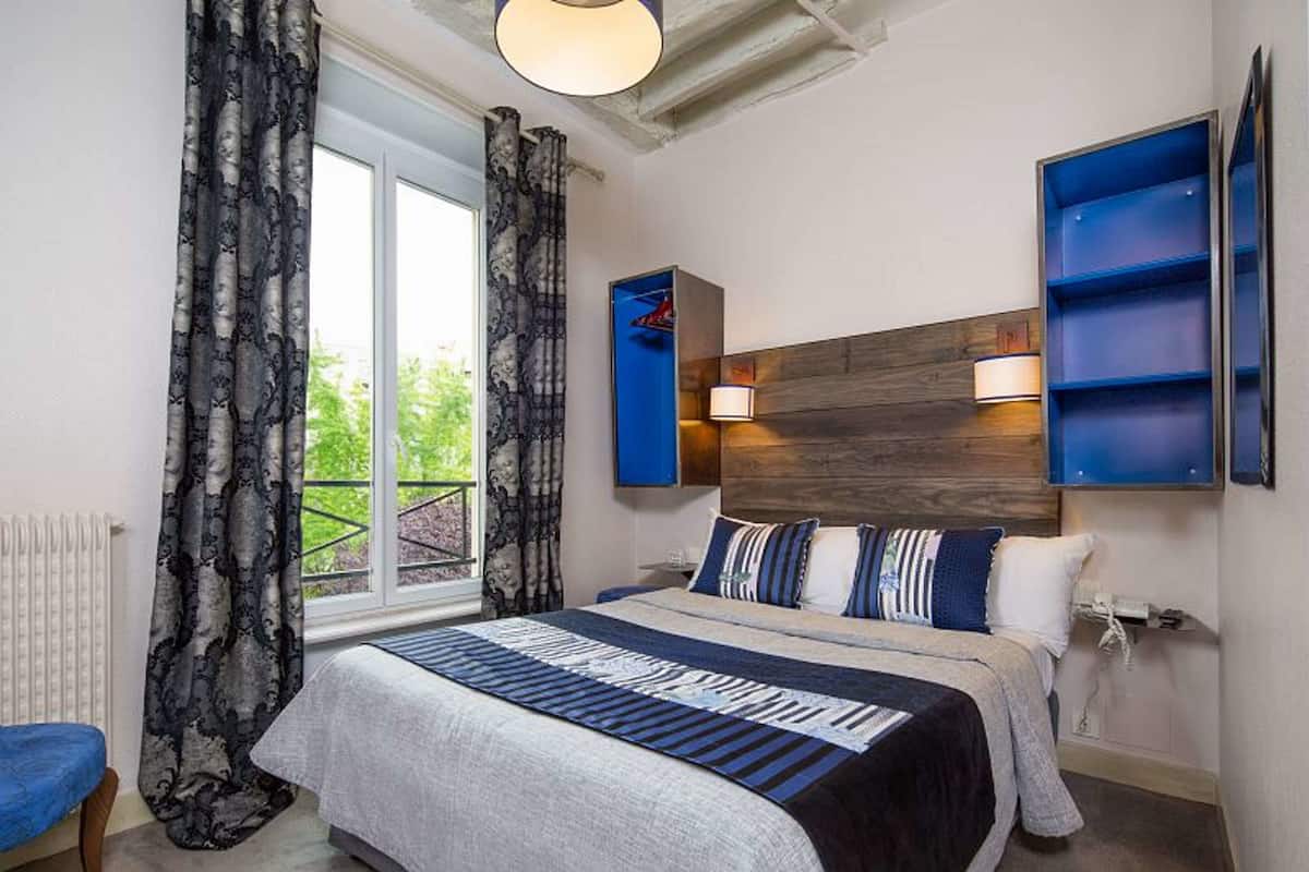 A bedroom with a large bed, a window with curtains, a blue shelving unit, and a wooden headboard.