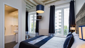 A hotel room with a bed, a TV, a window with curtains, and a view of buildings outside. - Hôtel Claret Bercy (Paris)