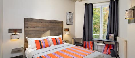 A bedroom with a wooden headboard, a bed with striped bedding, bedside lamps, a desk with a chair, and a window with curtains.