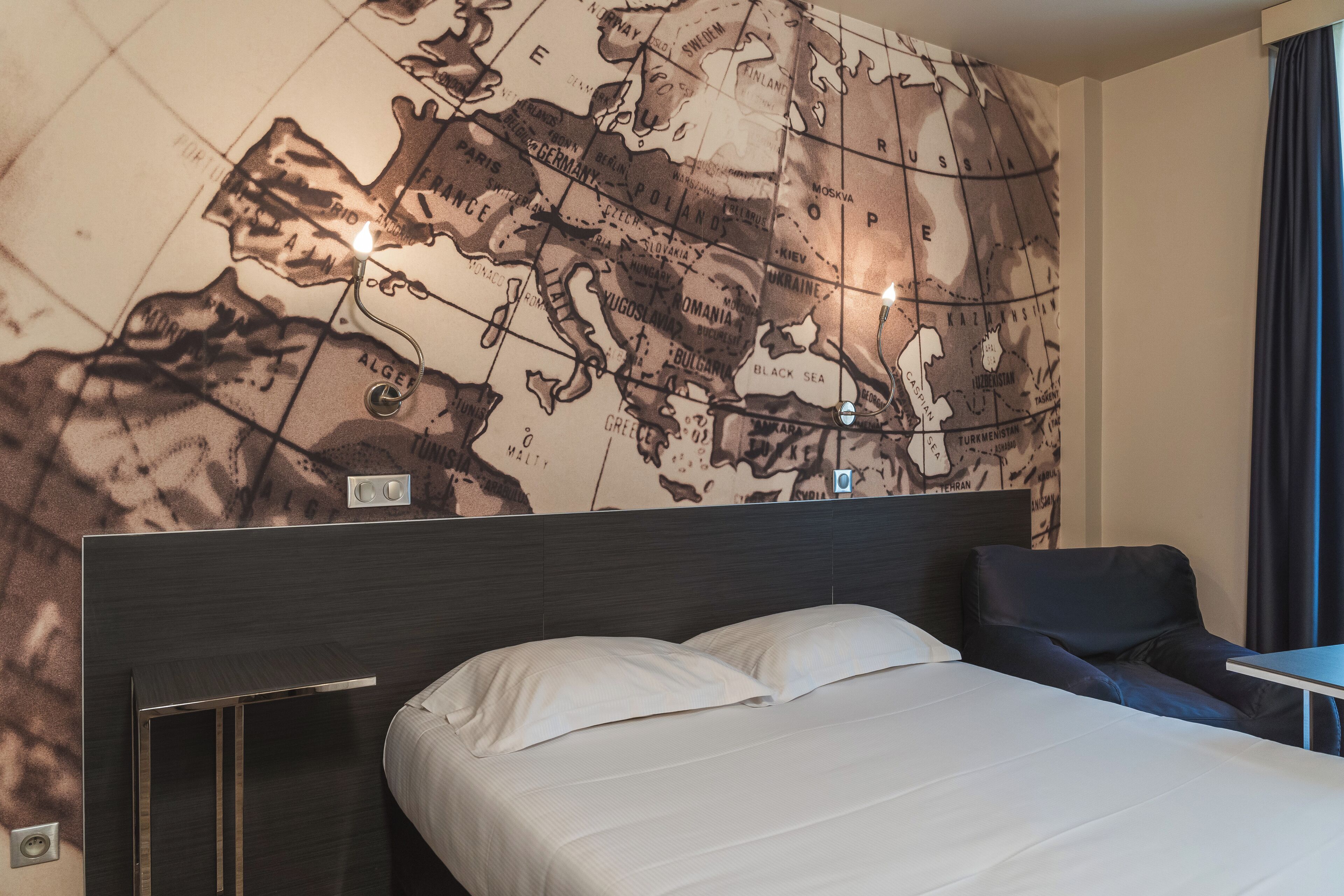 Une chambre d’hôtel avec une grande carte murale, un lit, un bureau et une chaise.
