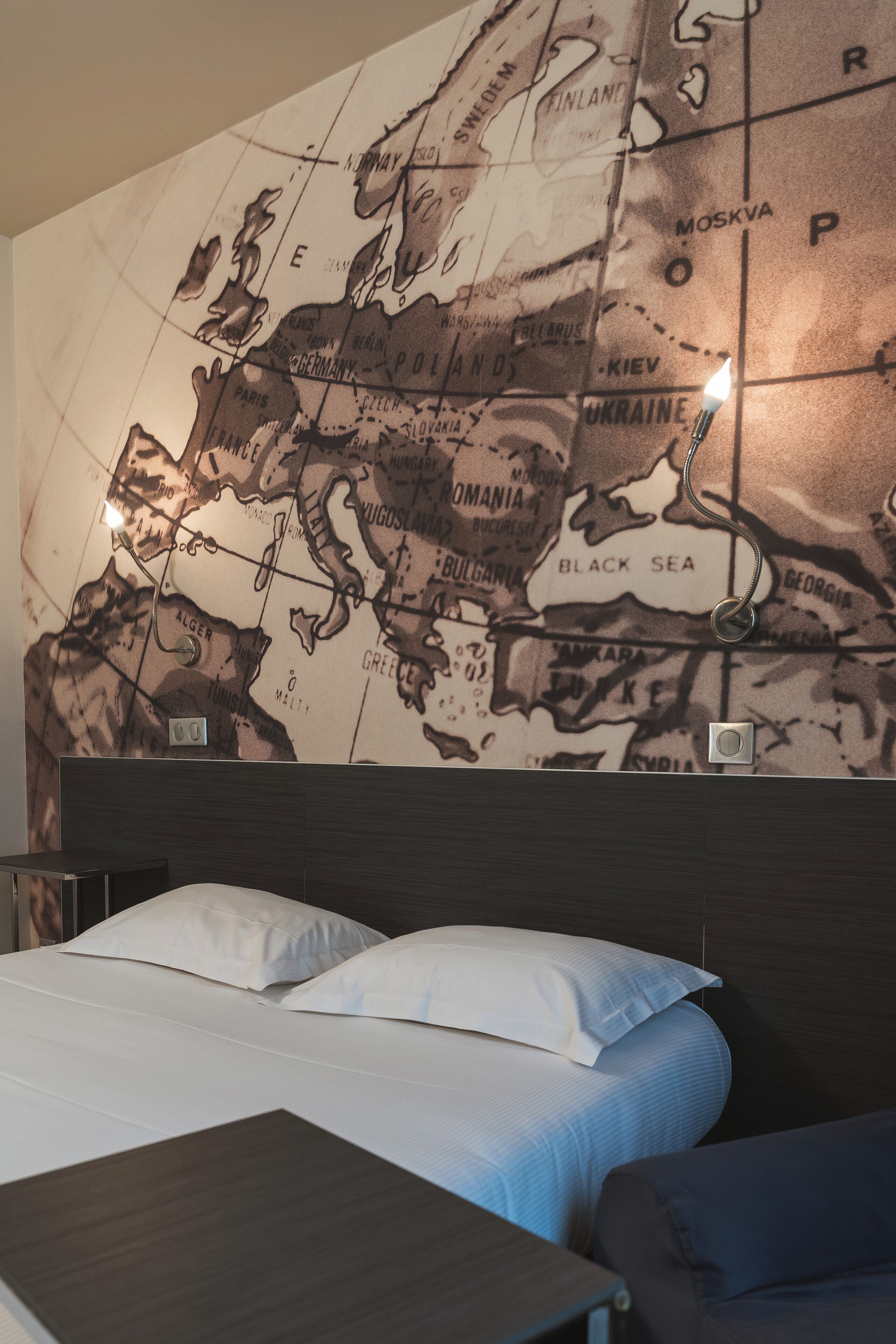 A hotel room with a large wall map, a bed with white bedding, and a wooden headboard.