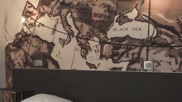 A hotel room with a large wall map, a bed with white bedding, and a wooden headboard.