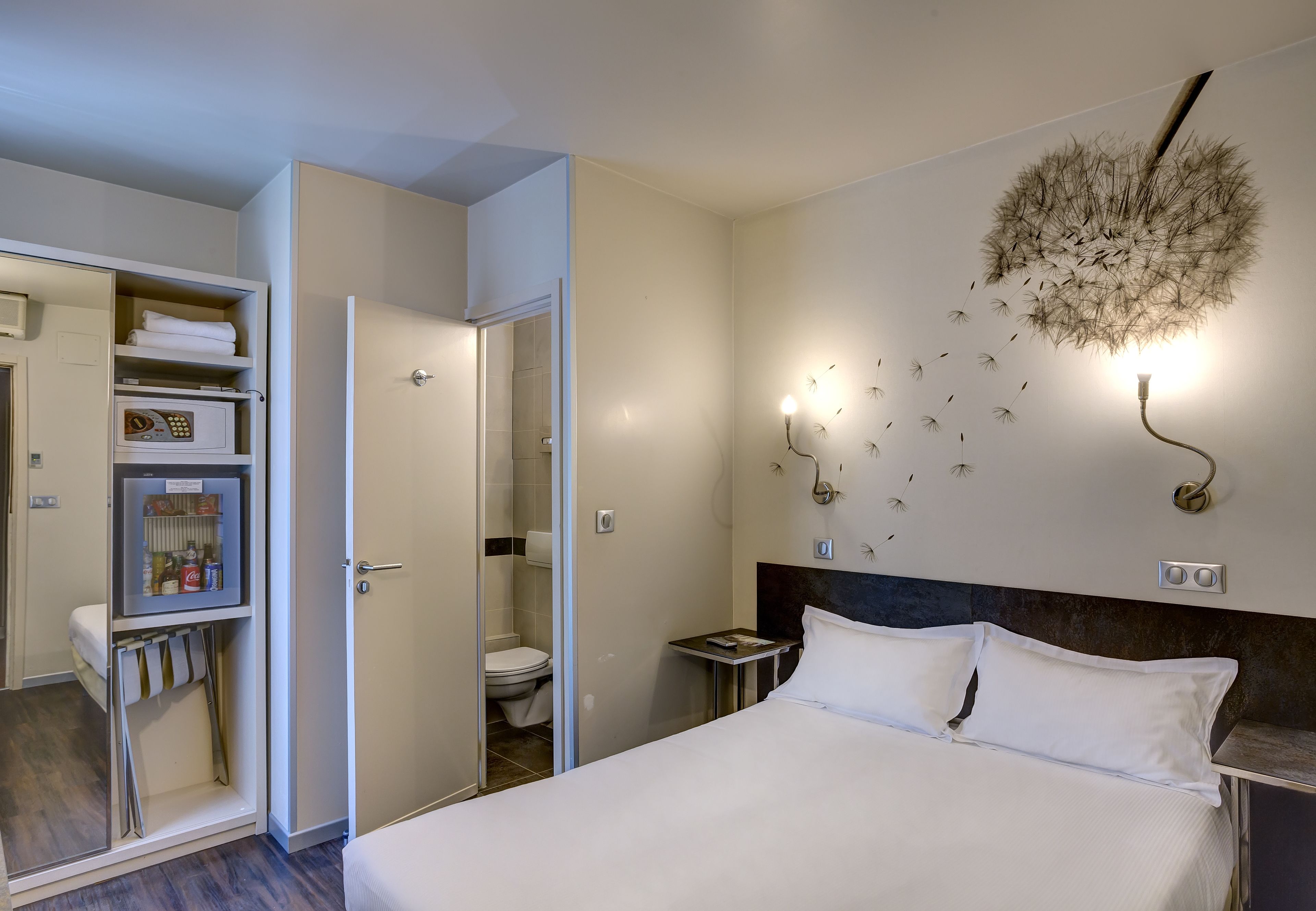 Een hotelkamer met een bed, nachtkastje, wandlamp en een kledingkast met planken.