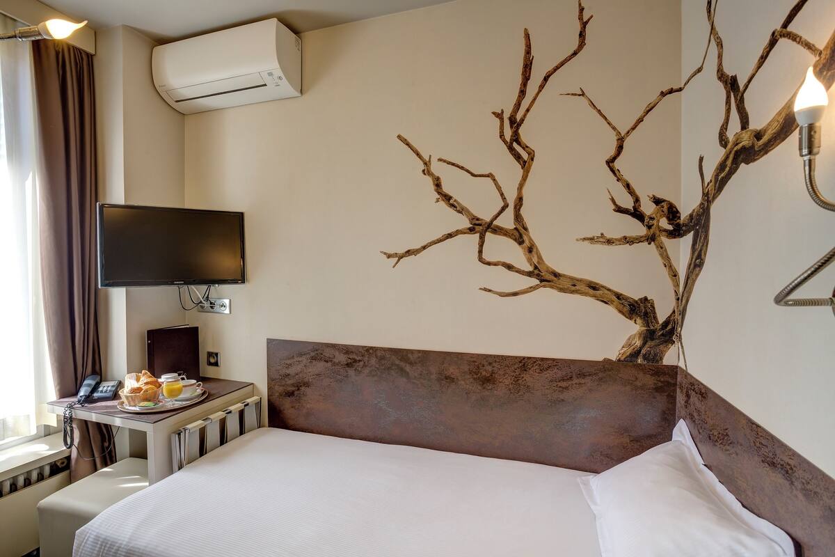 A hotel room with a bed, a desk with breakfast, a TV, and an air conditioner.