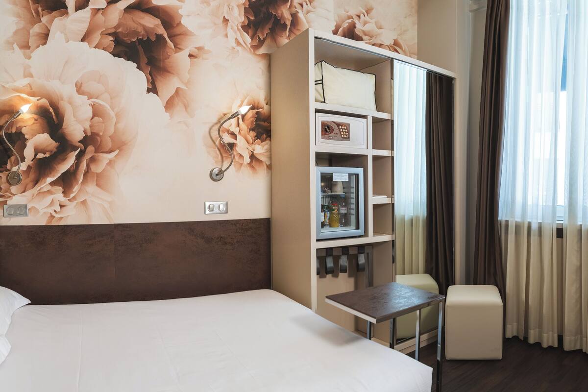 A hotel room with a large bed, a desk with a chair, a minibar, and a television.