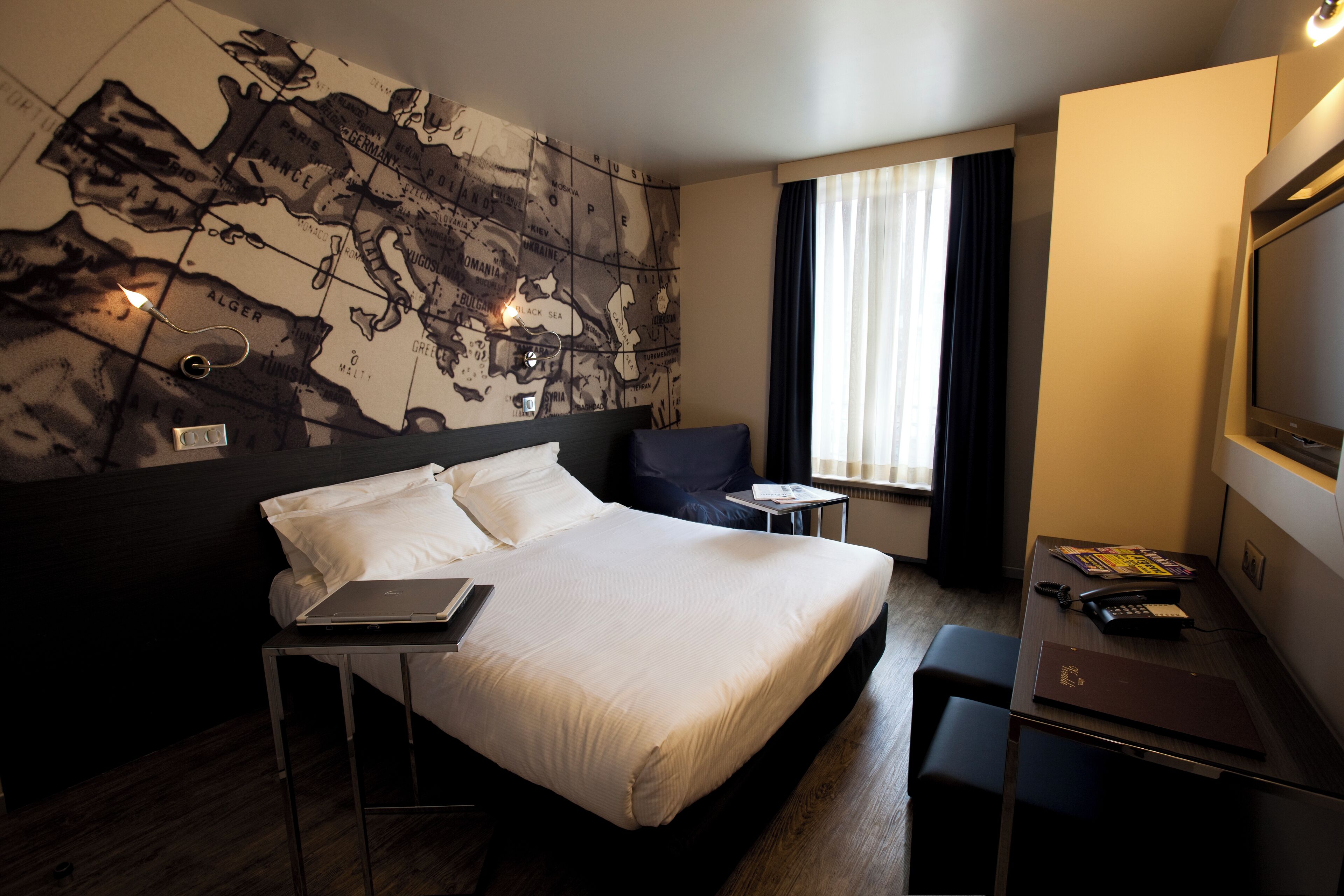 Une chambre d’hôtel avec un grand lit, un bureau avec un ordinateur portable, une chaise et une carte accrochée au mur.