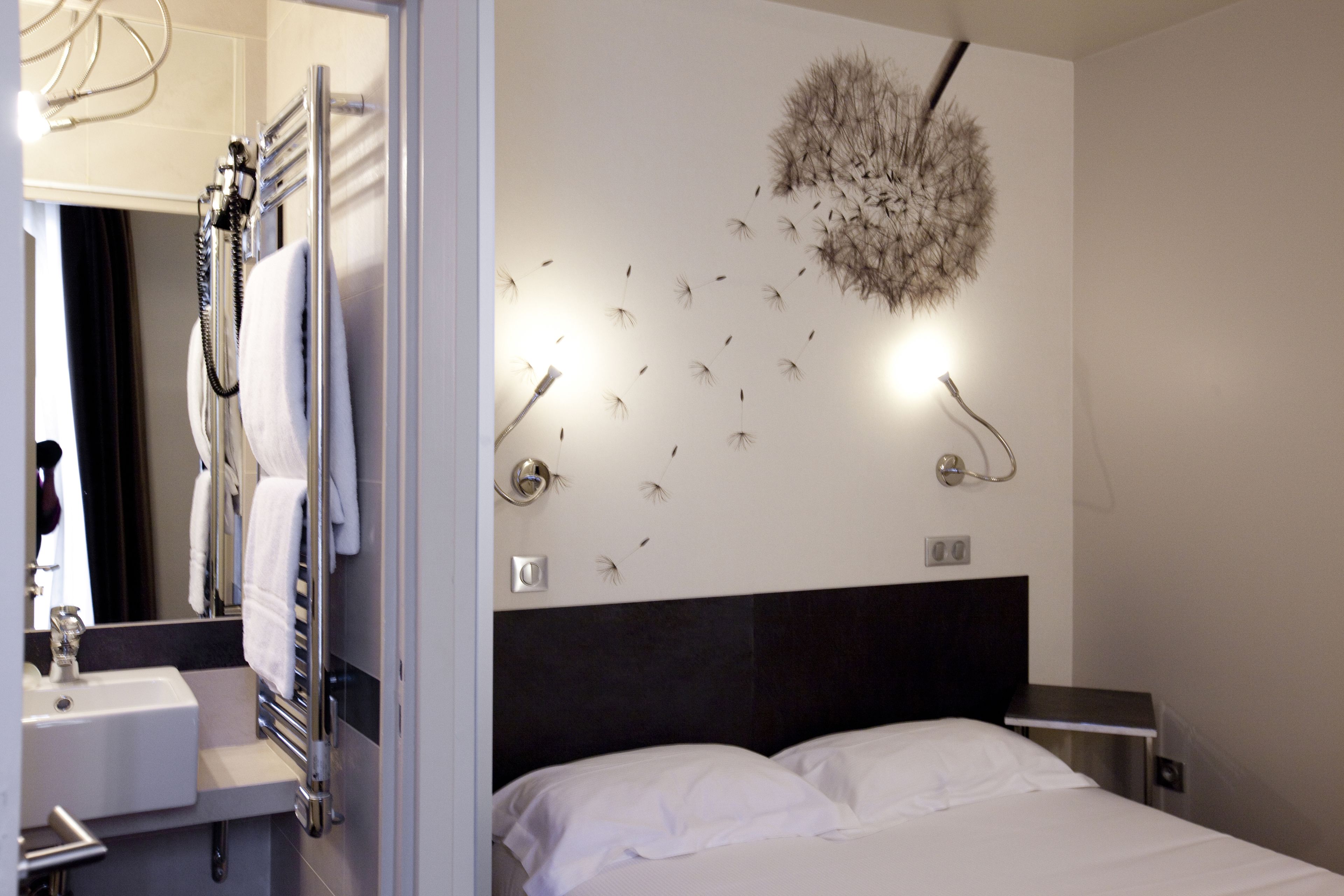 A hotel room with a bed, a bathroom with a sink and towel rack, and a wall-mounted light fixture.