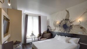 Ein Hotelzimmer mit einem großen Bett, einem Schreibtisch mit Stuhl, einem Fernseher und einem großen floralen Wandbild.