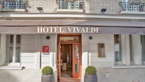 Der Eingang zum HOTEL VIVALDI mit einer braunen Markise, einem roten Schild und zwei großen Pflanzkästen.