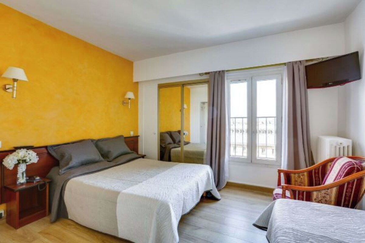 Una habitación de hotel con una cama, mesitas de noche, un televisor, una silla y una ventana con cortinas.