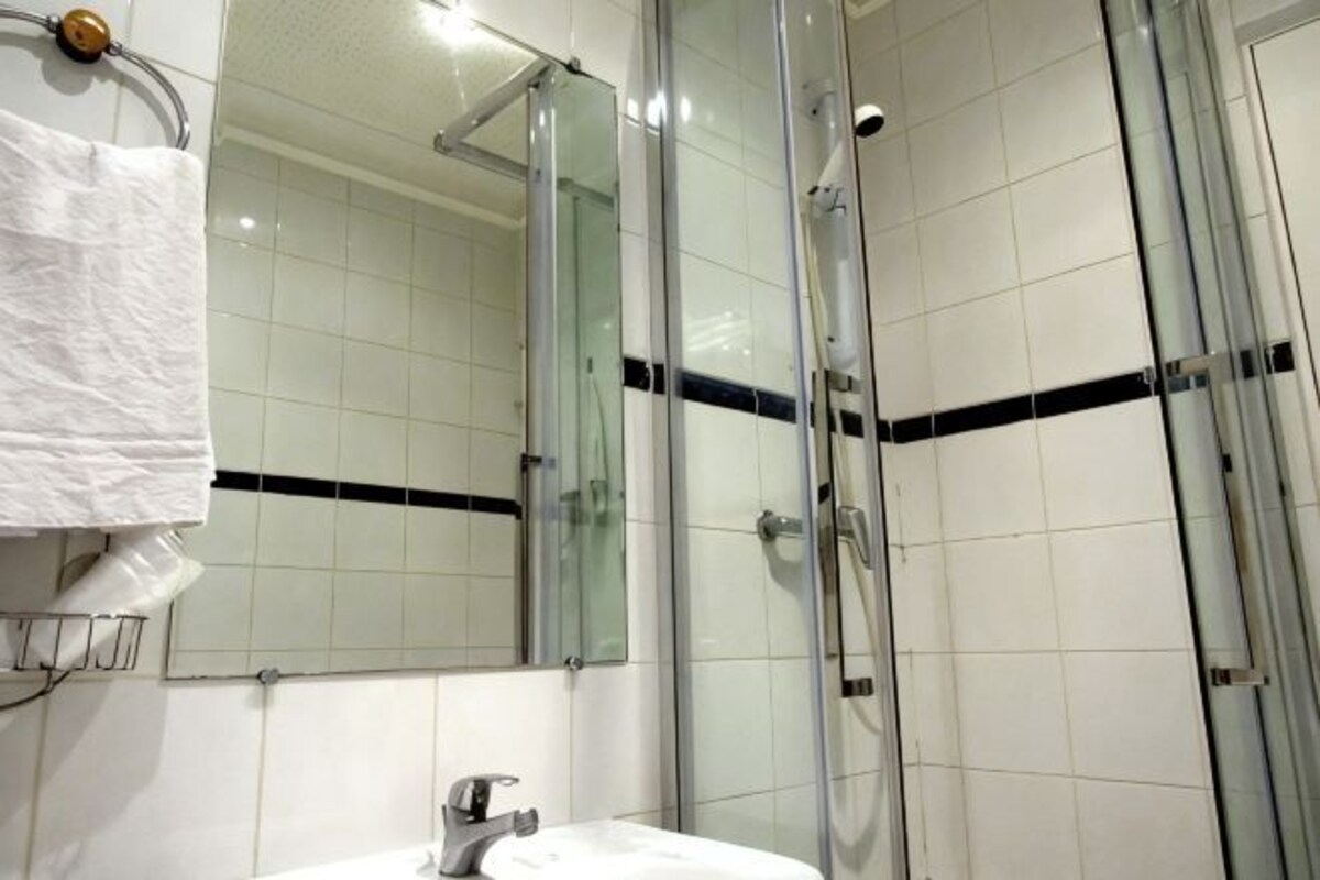 Een badkamer met een glazen douchecabine, een witte wastafel en een spiegel.