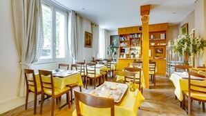 Un comedor con varias mesas y sillas, una estantería y una ventana con cortinas.