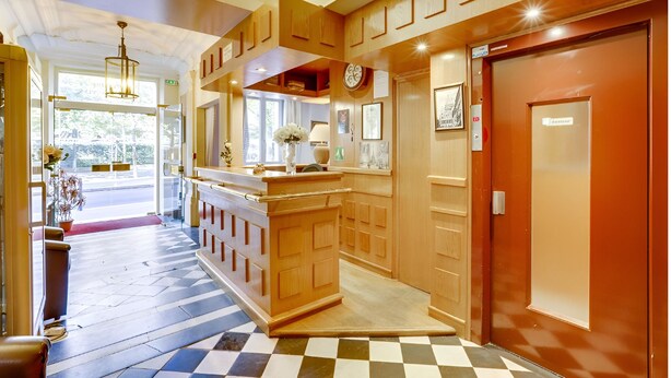 Un hall de hotel con piso a cuadros, paneles de madera, un mostrador de recepción y una puerta que indica 'Guest Room'.