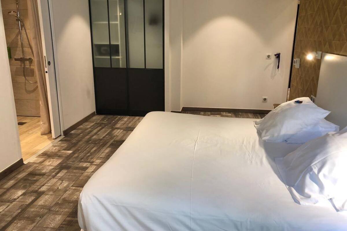Quarto de hotel com cama grande, piso de madeira, área de chuveiro e guarda-roupa de madeira.