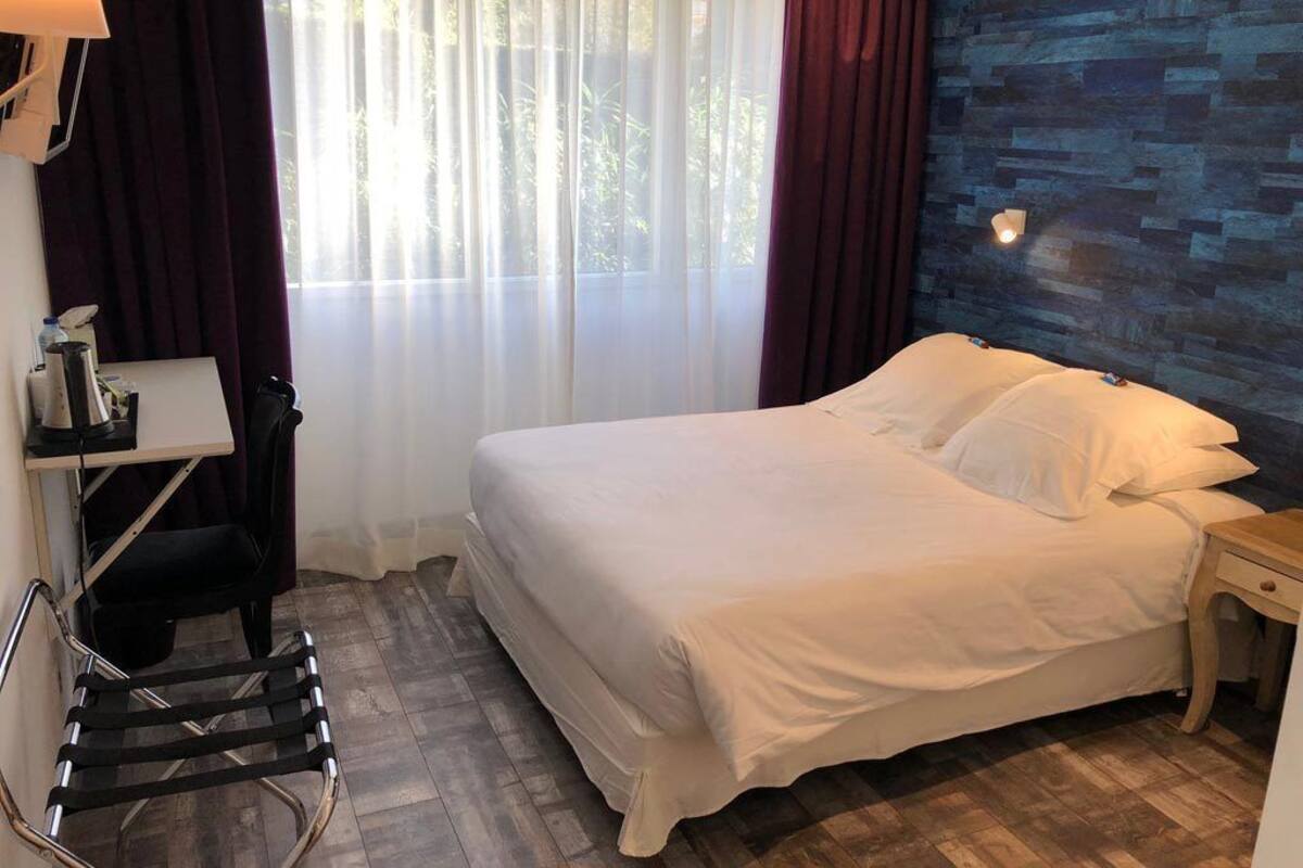 Quarto de hotel com cama, escrivaninha, cadeira e mesa de cabeceira.