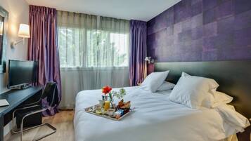 Une chambre d’hôtel avec un lit, un bureau équipé d’un ordinateur et un plateau de petit-déjeuner posé sur le lit.
