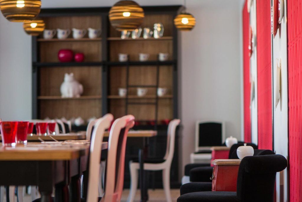 A restaurant interior with wooden tables, red chairs, and hanging pendant lights.