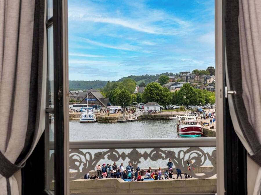 Vista desde una ventana con cortinas, con vista a un puerto con barcos y una multitud de gente.
