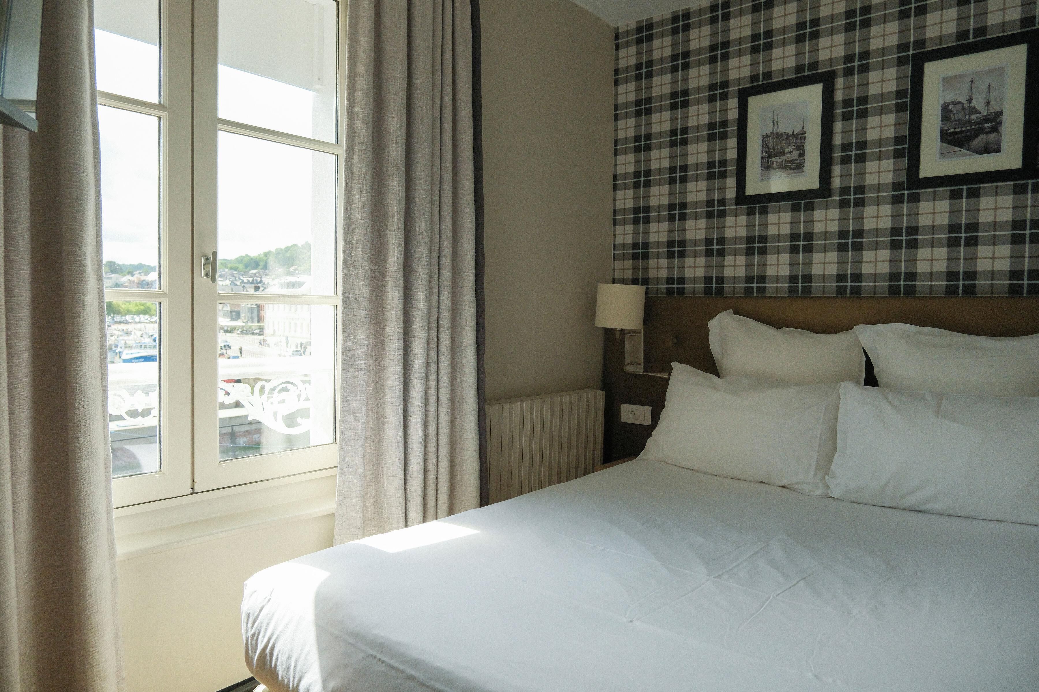 A hotel room with a bed, a window with curtains, a wall with a checkered pattern, and framed pictures.
