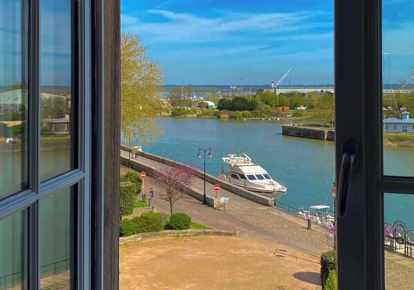 A view of a river with a boat docked on the right, a pedestrian bridge, and a clear sky. - Best Western Le Cheval Blanc - Vieux Port (Honfleur)