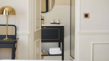 A hotel room with a bed, a bedside table with a lamp, a black and gold vanity with a mirror, and a towel rack.