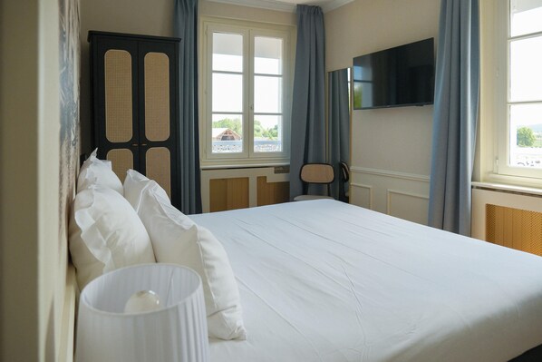 Une chambre d’hôtel avec un lit, un téléviseur fixé au mur, une fenêtre avec des rideaux et une vue sur l’extérieur.