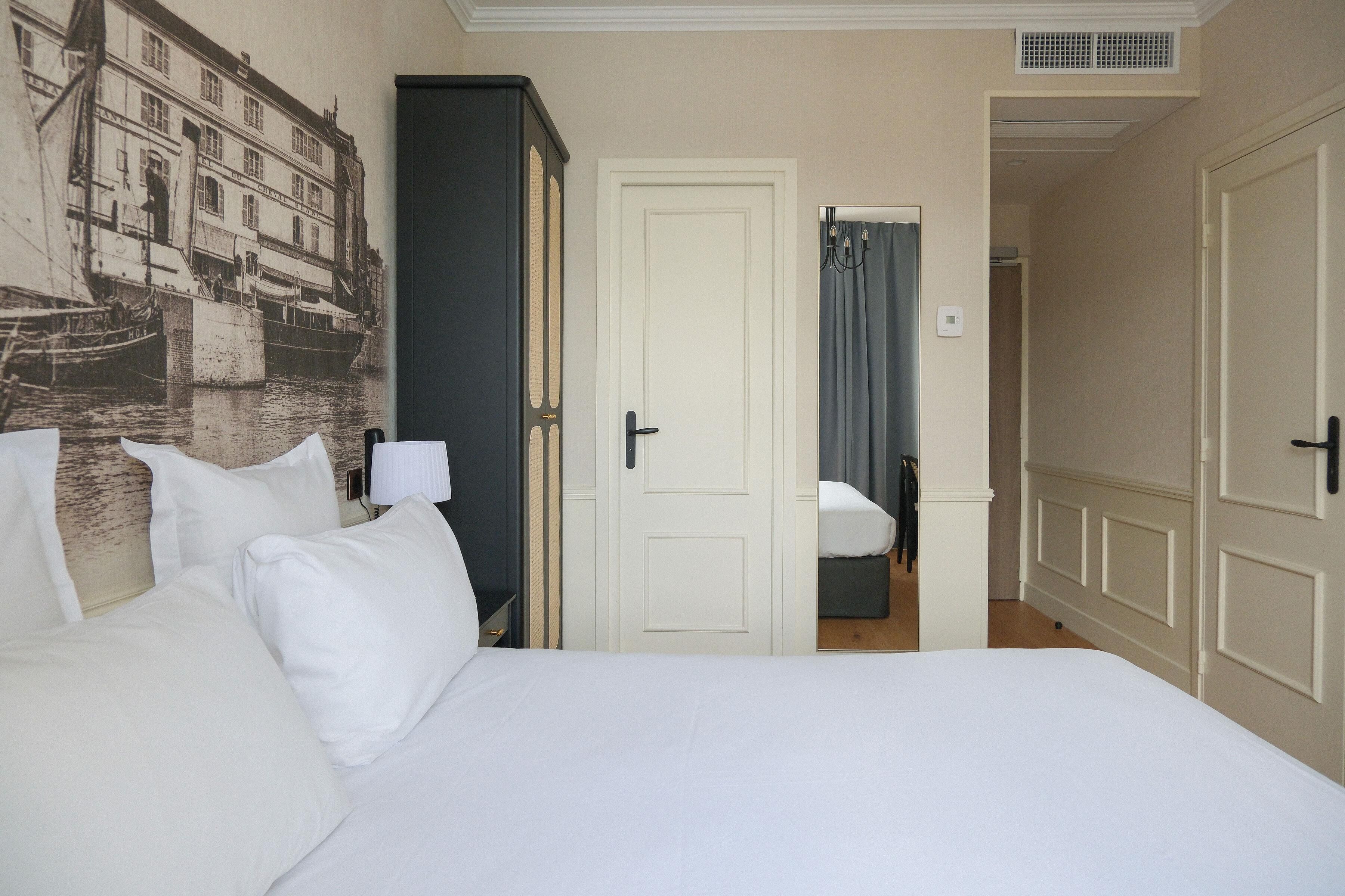 A hotel room with a bed, a wardrobe, a door leading to another room, and a wall with a historical building mural.