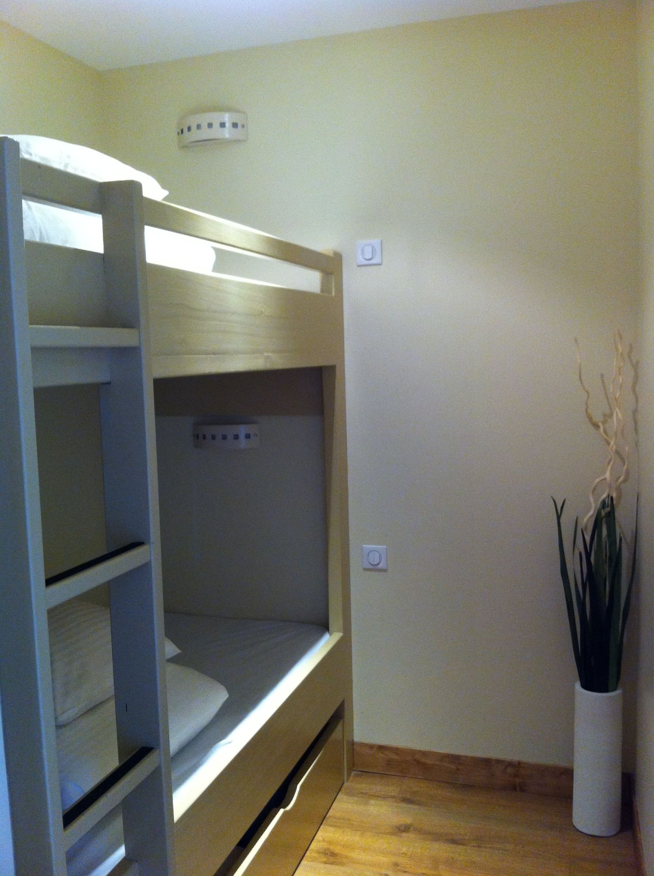 Een stapelbed in een kamer met een houten vloer, een wandairconditioner en een bloempot.