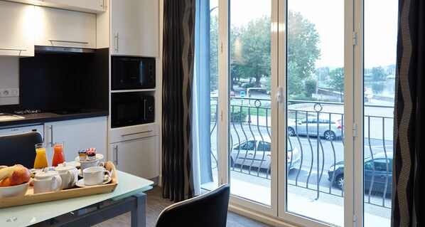Une chambre d’hôtel dotée d’un coin repas, d’une kitchenette et offrant une vue sur la rue grâce à de grandes fenêtres.