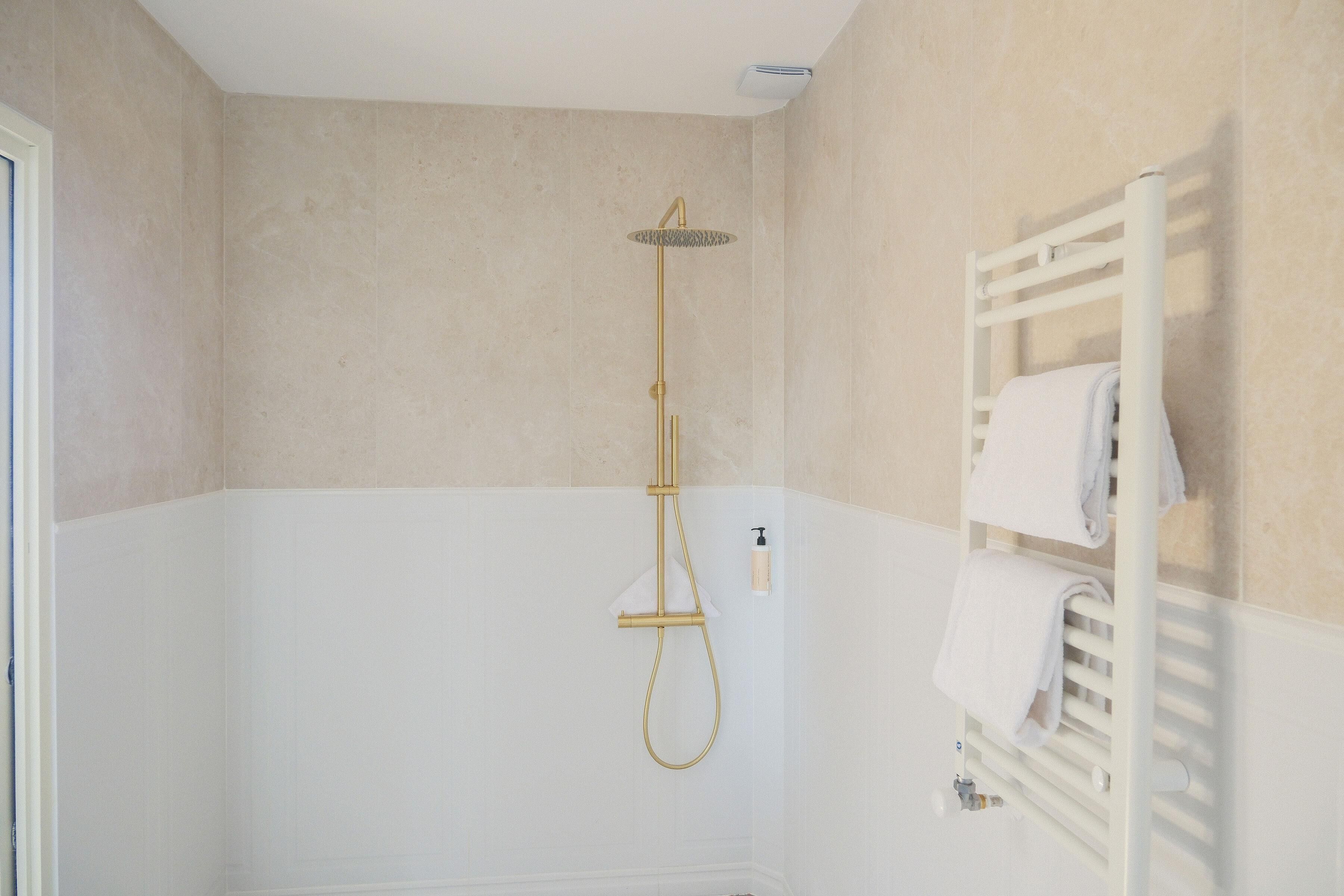 A bathroom with a white bathtub, a gold showerhead, and a white towel rack.