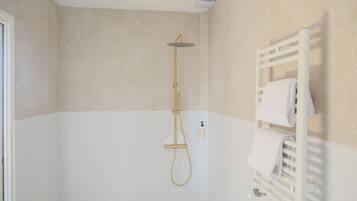 Un baño con una bañera blanca, un cabezal de ducha dorado y un perchero blanco.