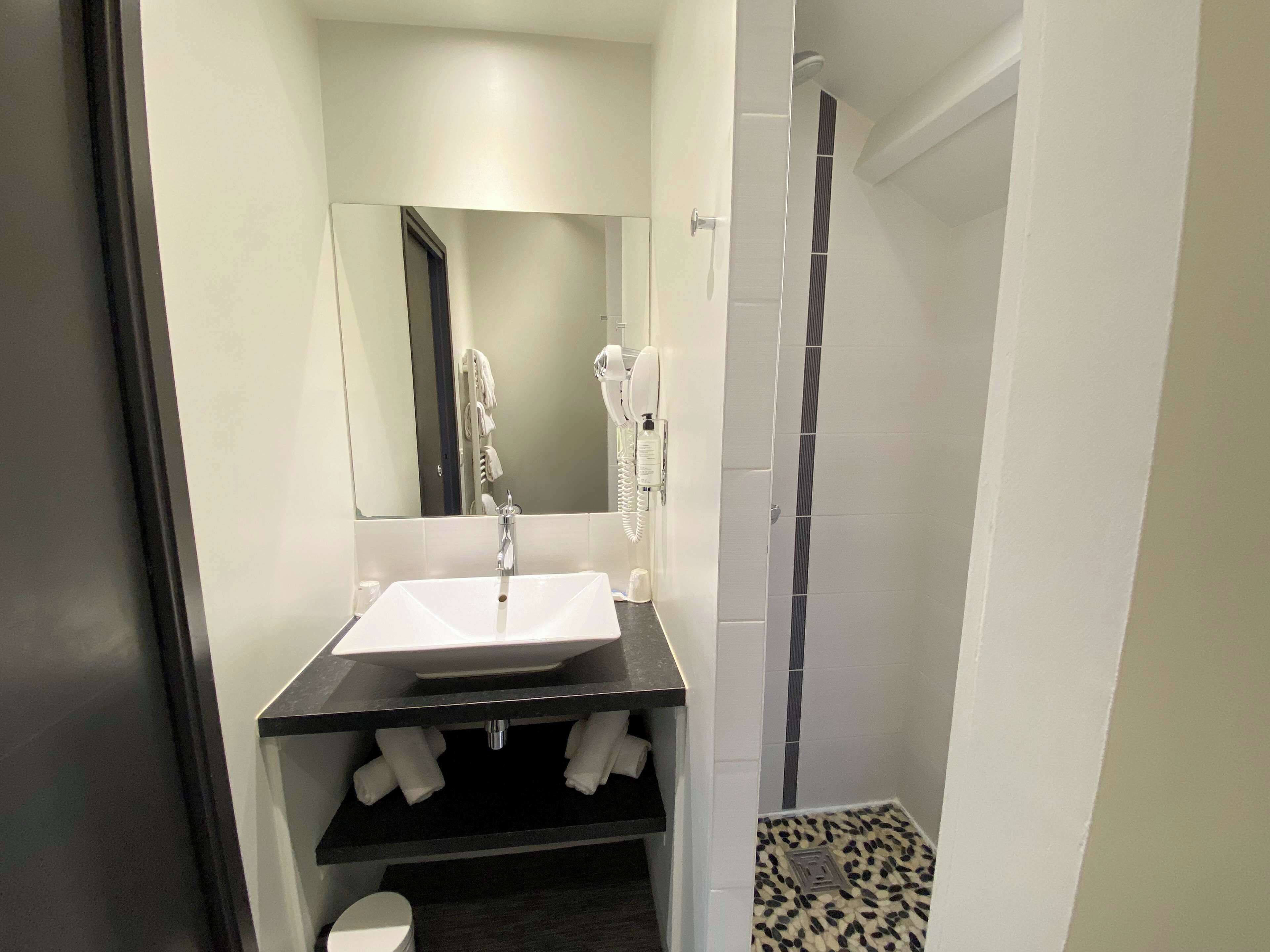 Un baño moderno con un lavamanos blanco, un espejo encima, un perchero y una zona de ducha.