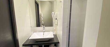 Un baño moderno con un lavamanos blanco, un espejo encima, un perchero y una zona de ducha.