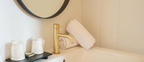 A bathroom with a white sink, gold faucet, and a mirror. There are two toiletries on the sink's edge.
