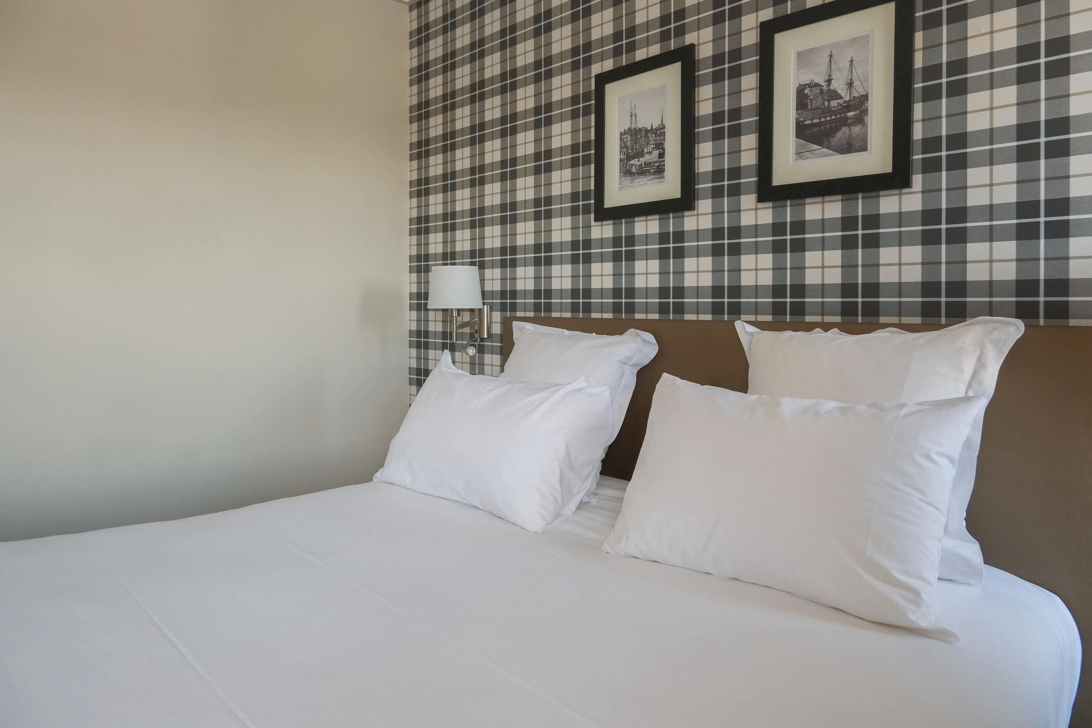 A hotel room with a bed, two pillows, a nightstand with a lamp, and a checkered wall.
