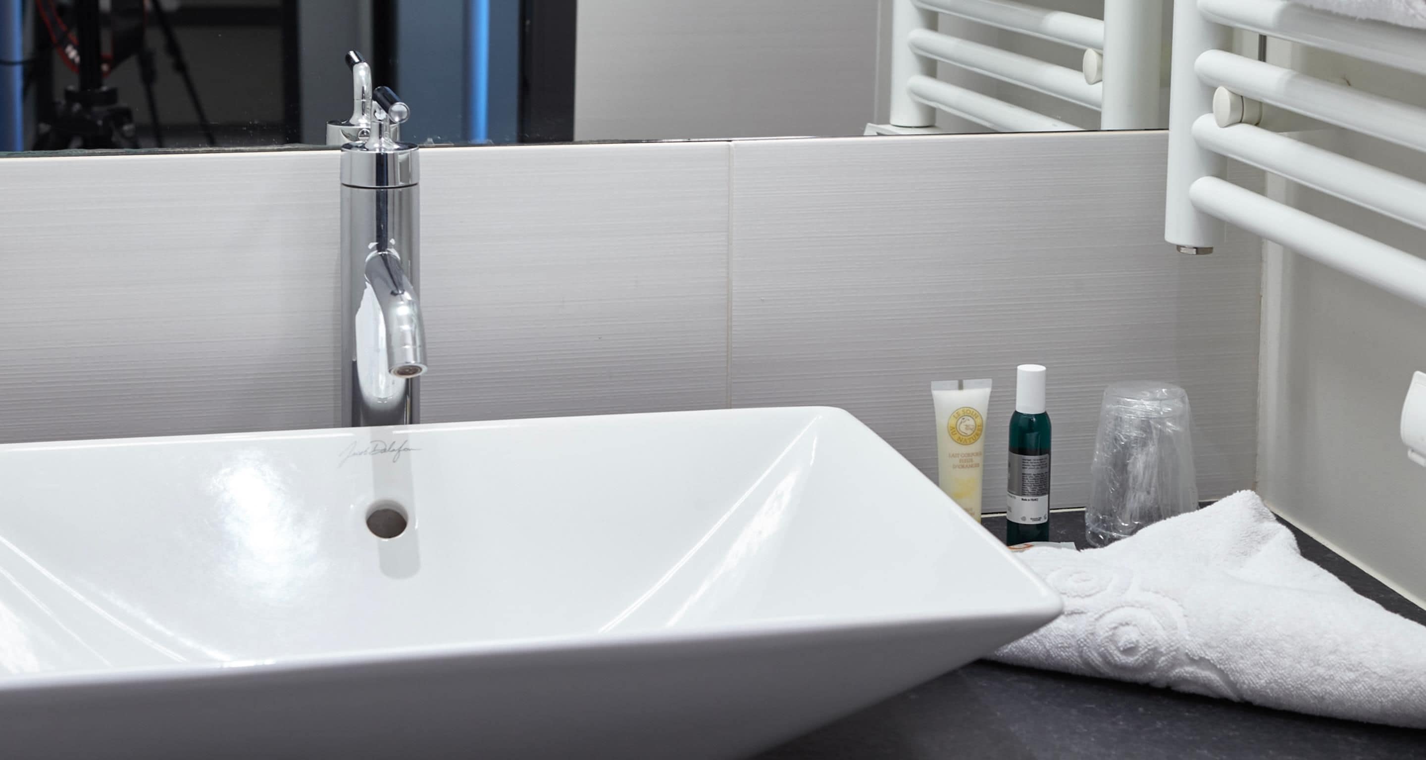 Uma pia de banheiro branca com uma torneira cromada, uma toalha e produtos de higiene no balcão.