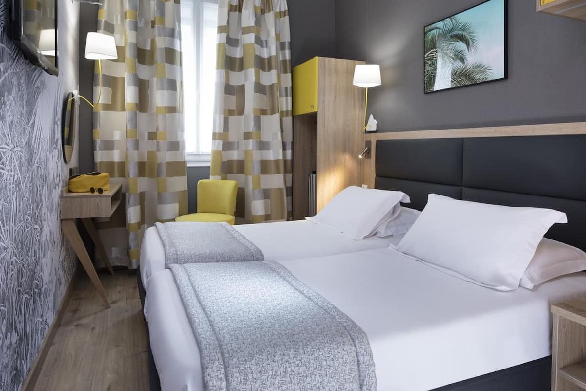 Habitación de hotel con una cama grande, una mesita de noche, una silla, un escritorio y un espejo.