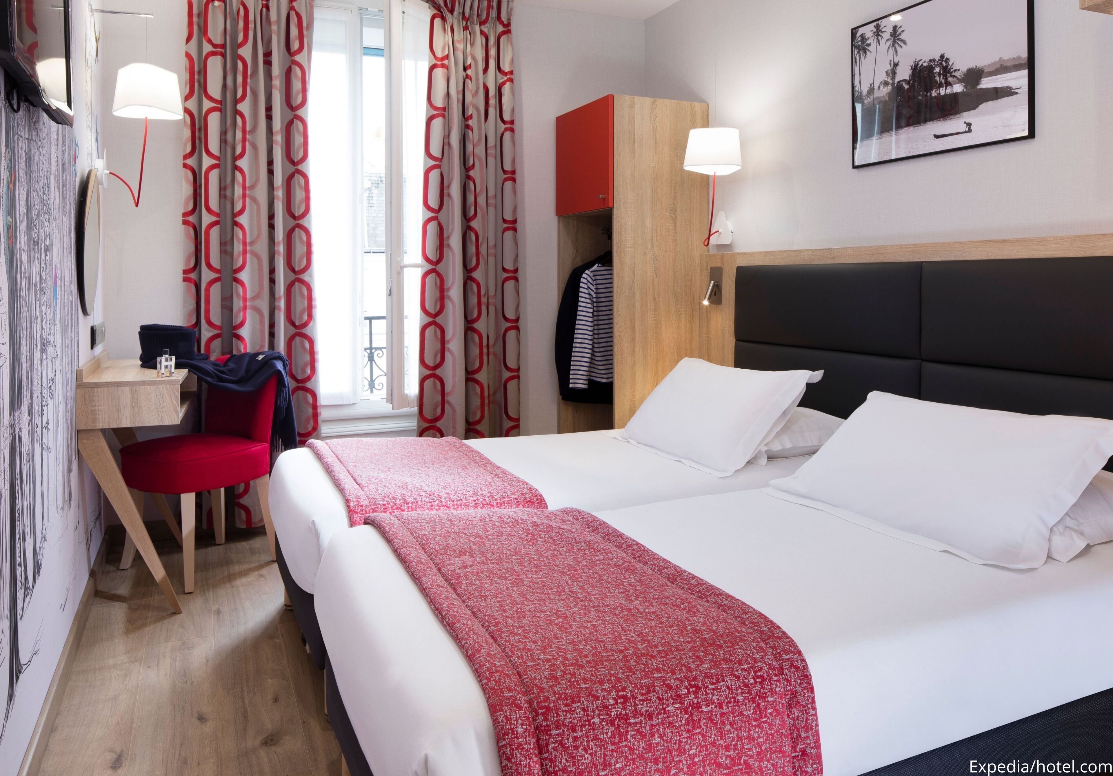 A hotel room with a bed, a desk, a chair, a wardrobe, and a window with curtains.