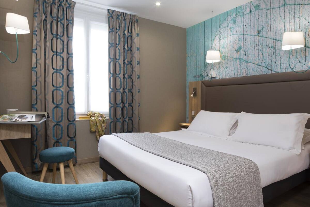 Una habitación de hotel con una cama grande, un escritorio con una silla y una ventana con cortinas.