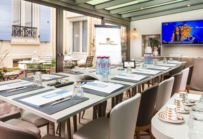 A conference room with a long table set for a meeting, a television displaying a weather forecast, and a sign for Hotel de Tamers. - Hôtel Daumesnil - Vincennes (Vincennes)