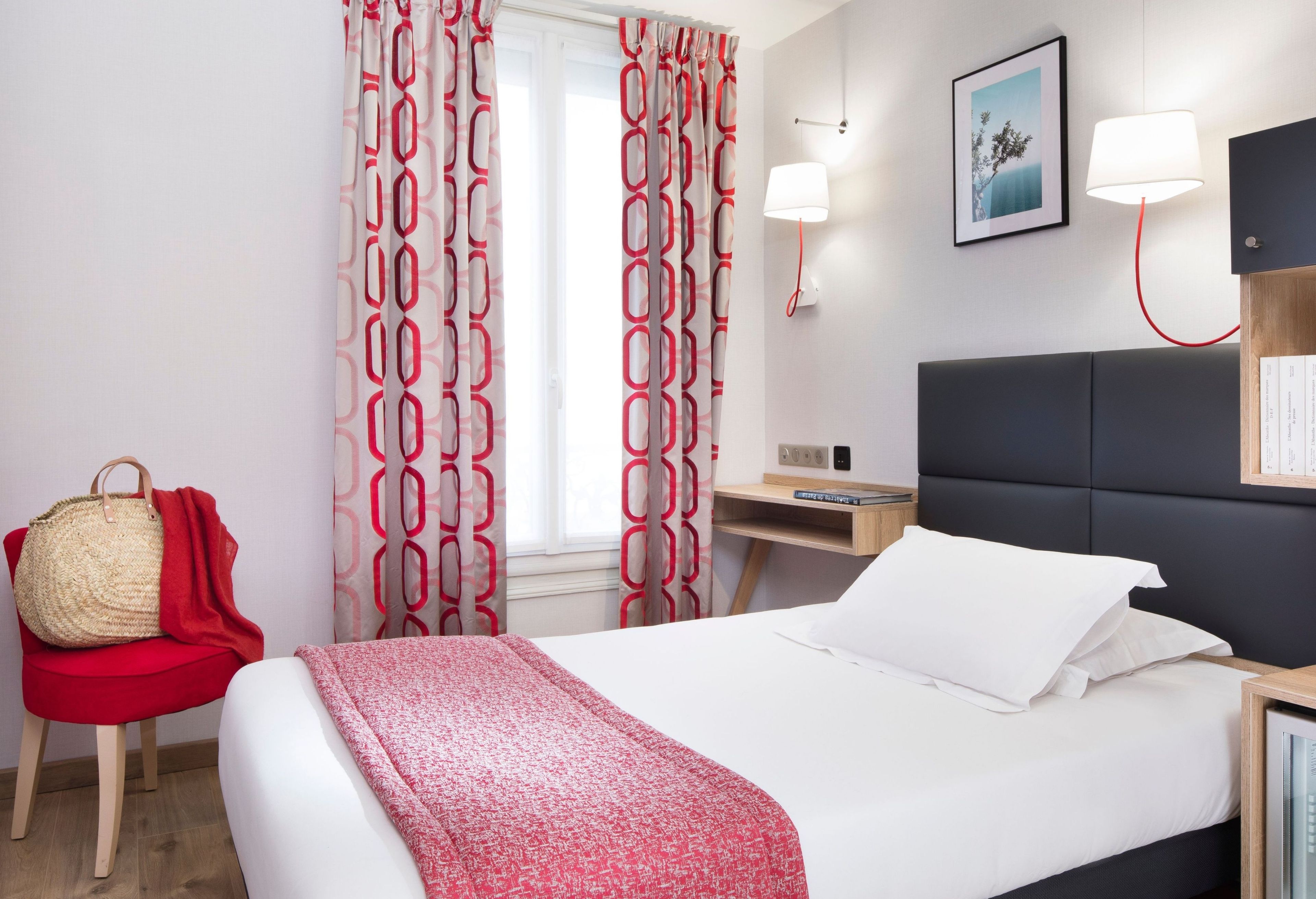 Ein Hotelzimmer mit einem Bett, einem Nachttisch, einer Lampe, einem Sessel, einem Wandregal und einem Fenster mit Vorhängen.