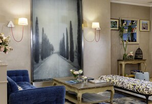 A room with a large abstract painting, a sofa, a small table with books and flowers, a blue armchair, and a bookshelf with books and decorative items. - Hôtel Daumesnil - Vincennes (Vincennes)