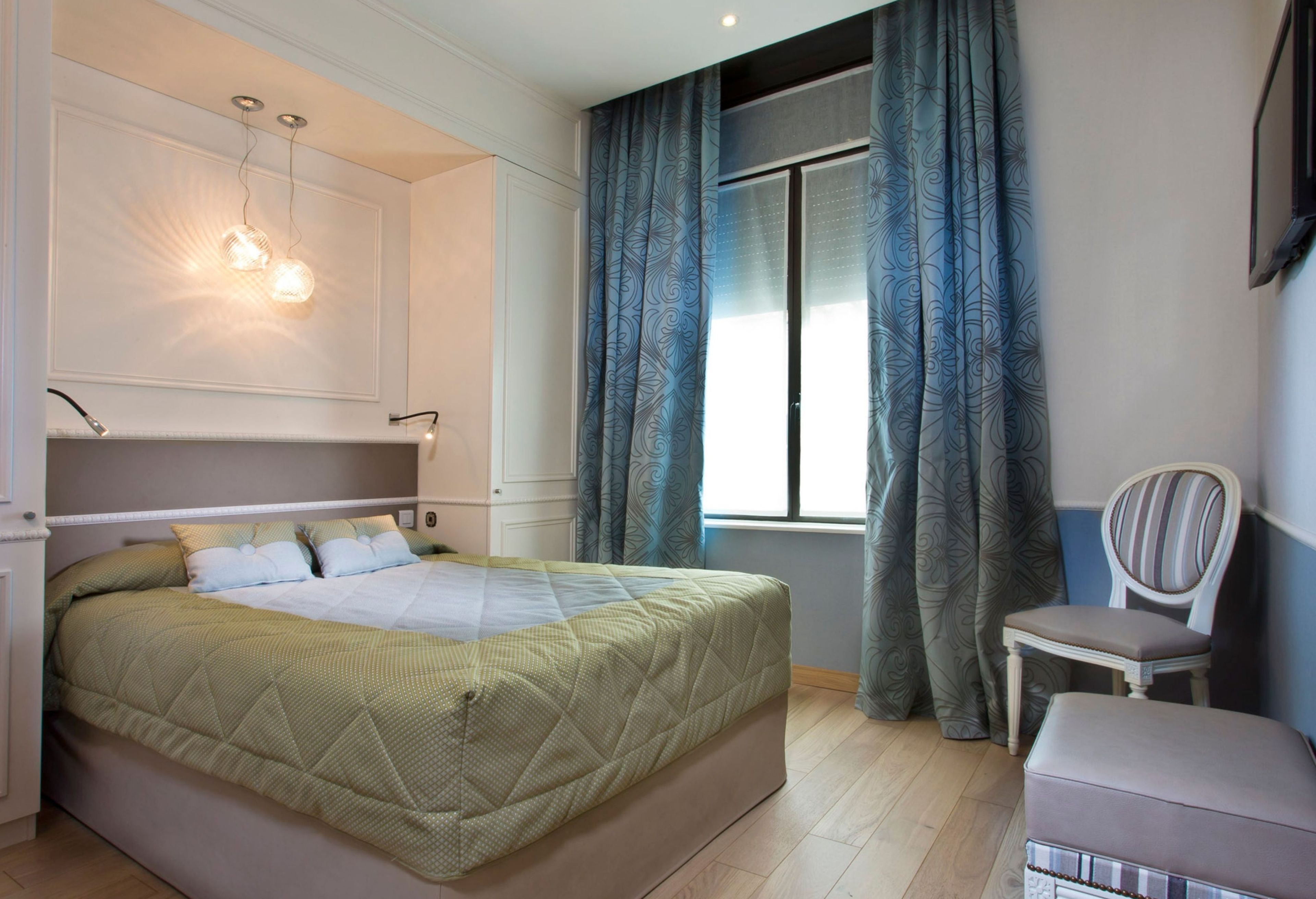 A bedroom with a bed, a chair, a desk, and a window with curtains.